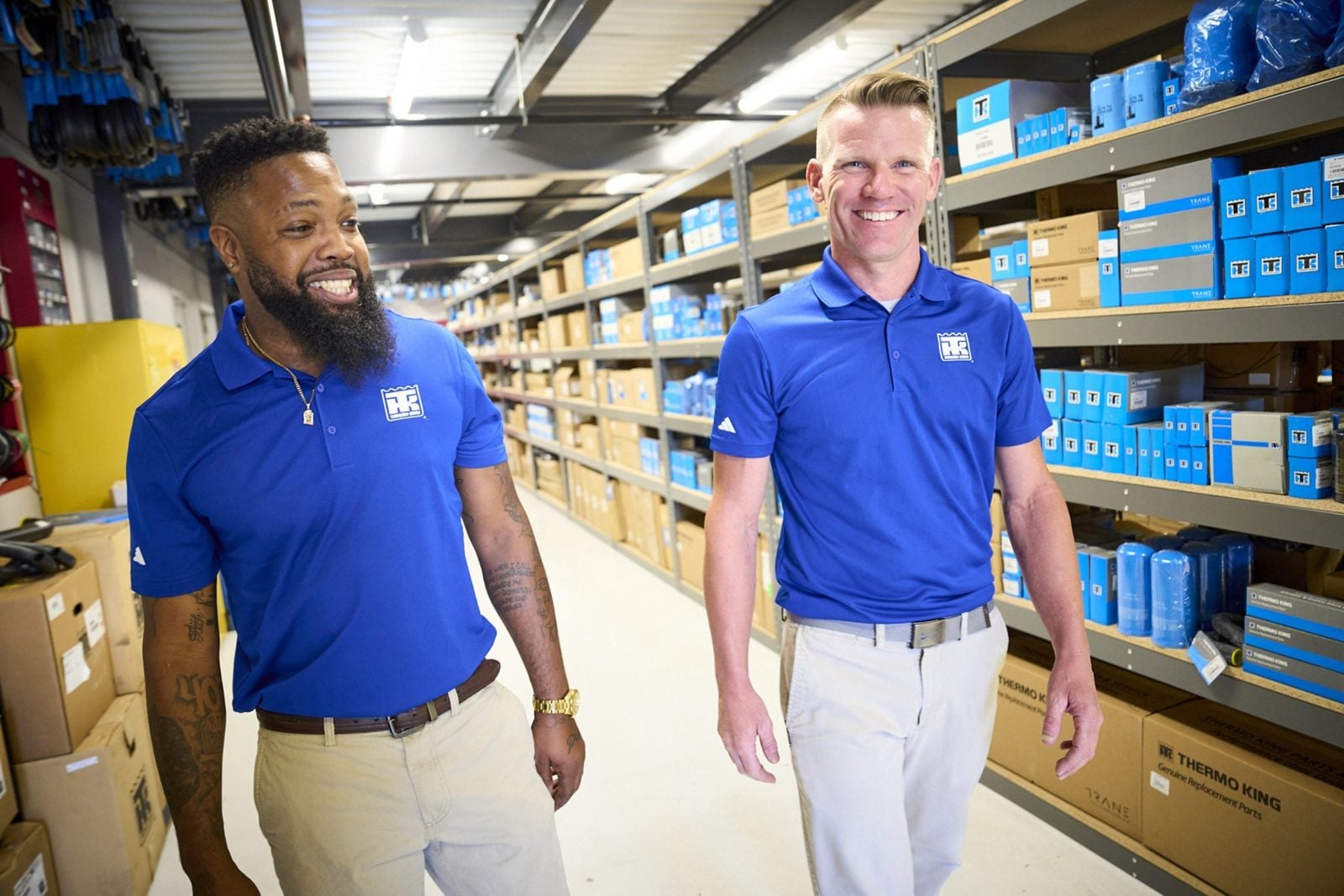 Two people in Thermo King shirts walking down an aisle of parts shelves