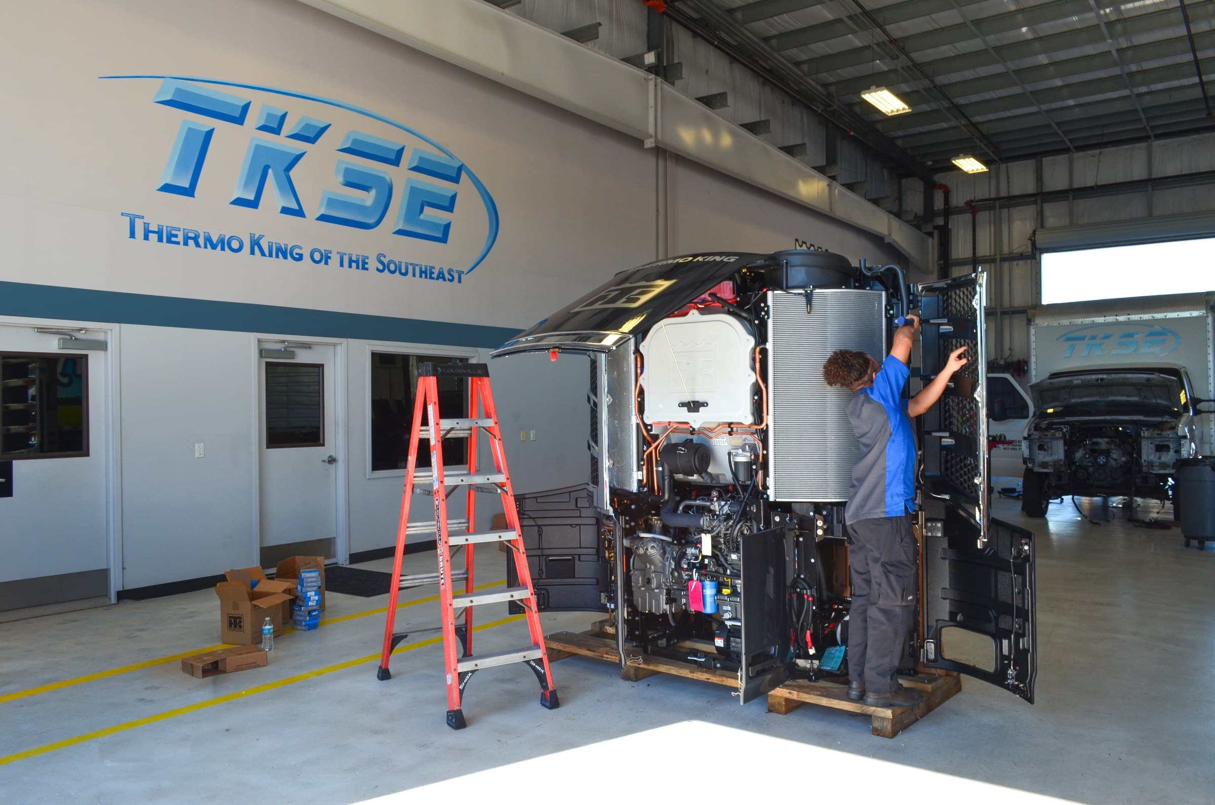 A TKSE technician servicing an open Thermo King unit in a TKSE shop