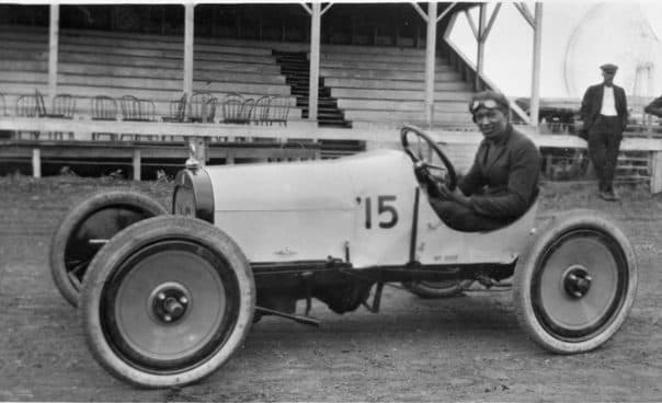 An early race car, number 15, with its driver at the wheel