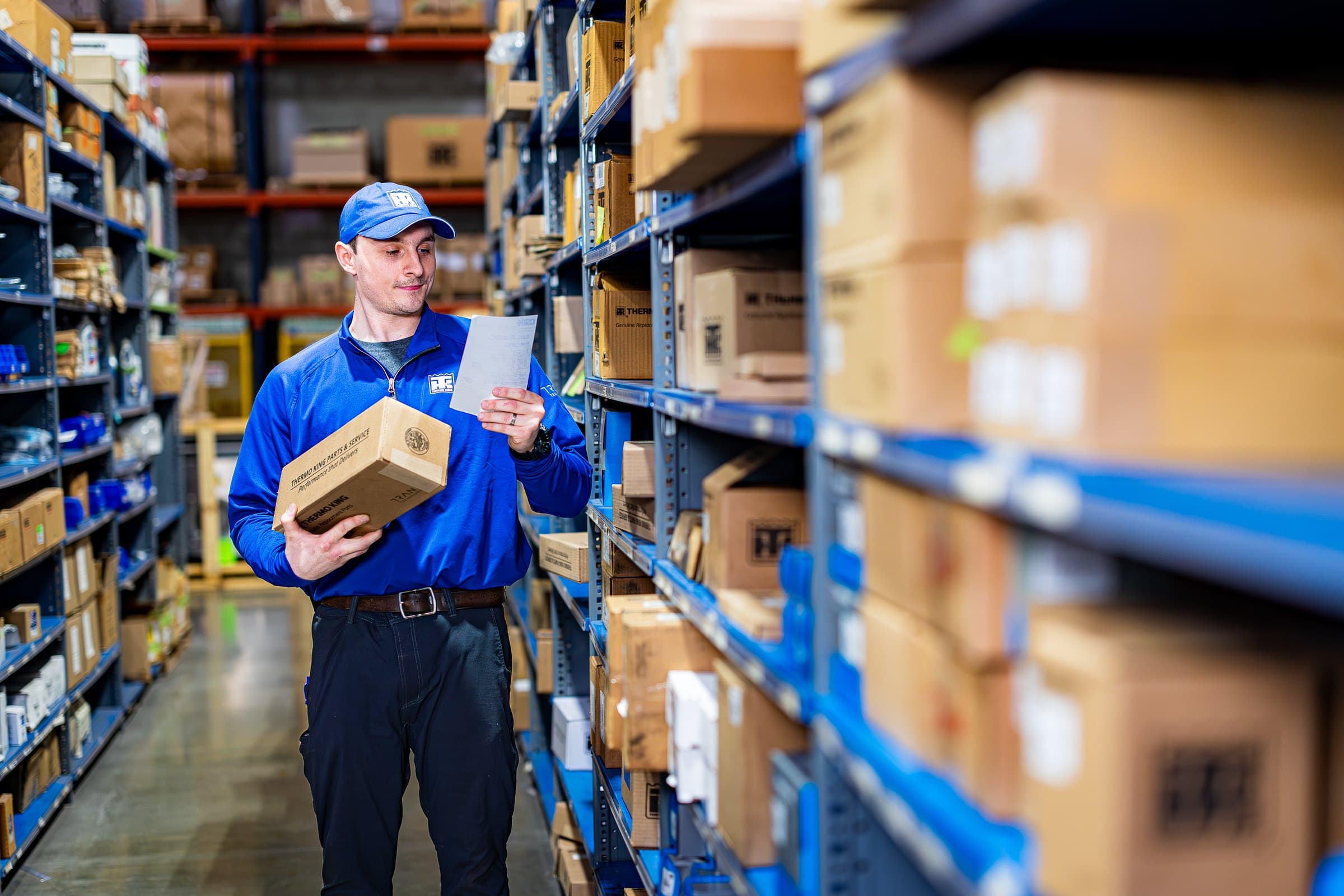 A Thermo King parts specialist holding a box in a parts warehouse aisle