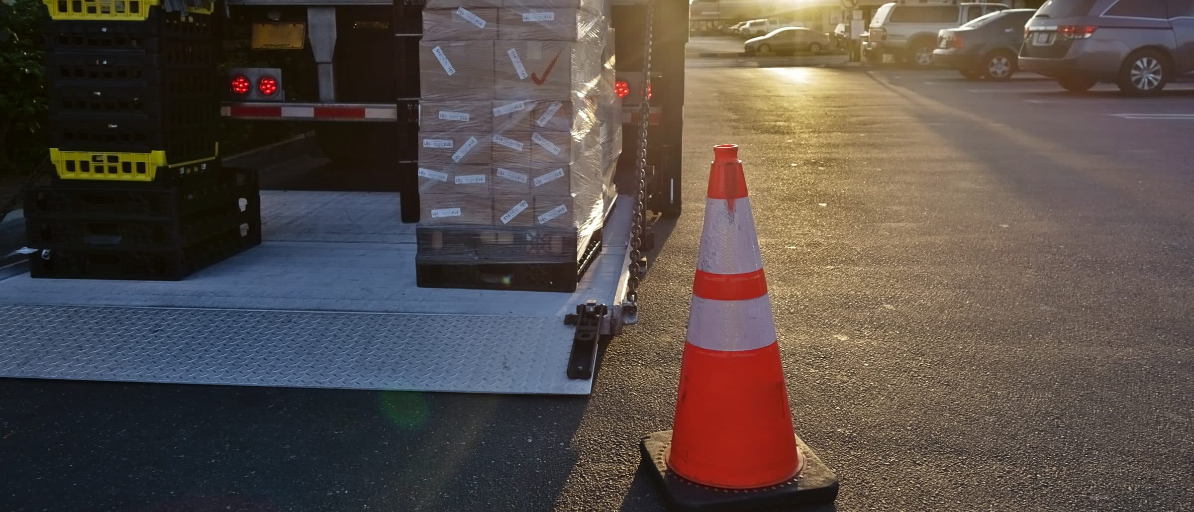 A liftgate platform lowered to the pavement behind a delivery trailer, loaded with crates and a wrapped pallet