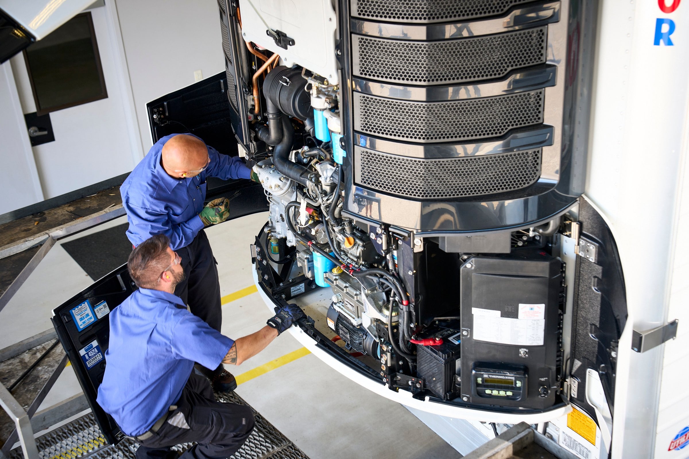 Two technicians working on an opened-up Thermo King Precedent trailer unit