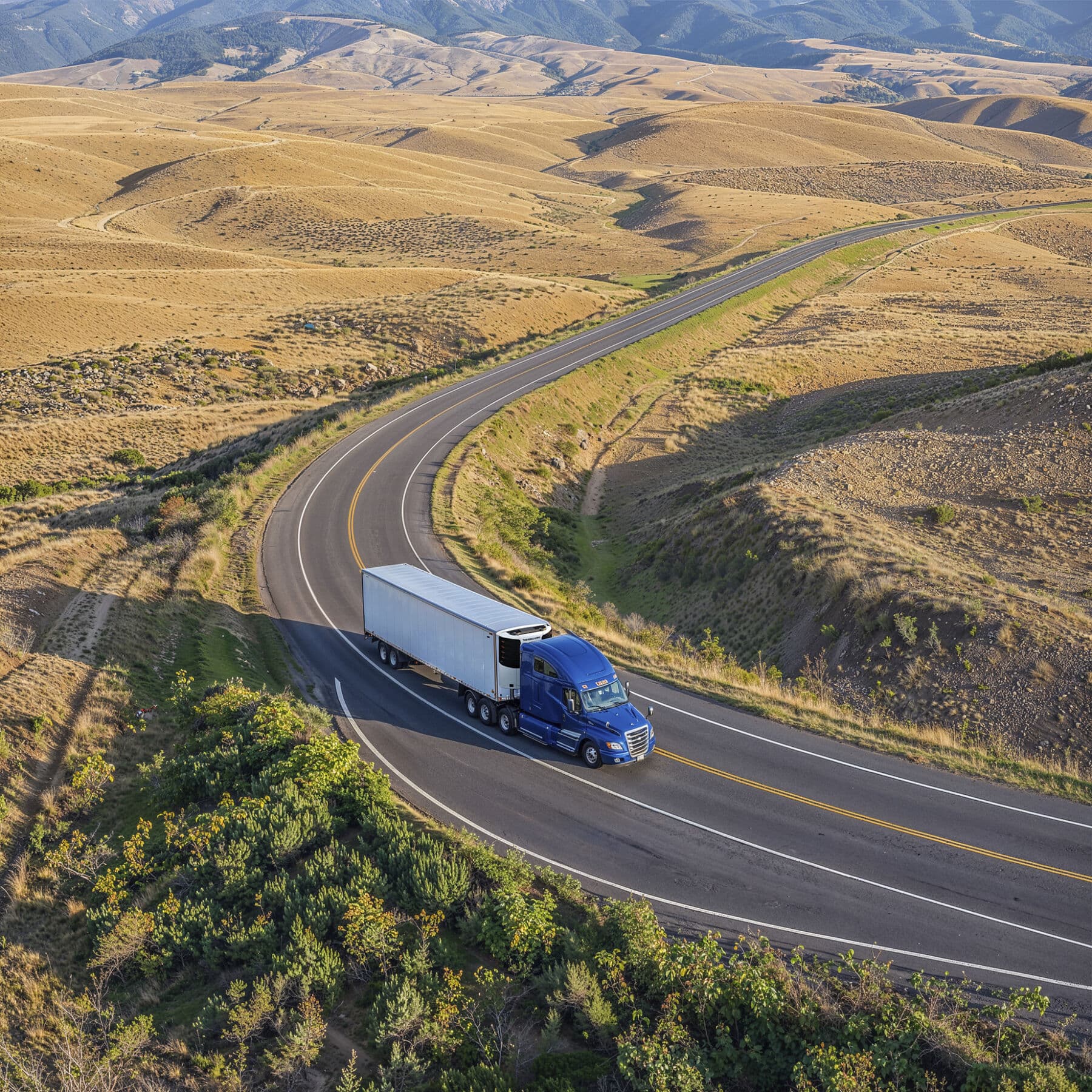 A tractor-trailer with a Thermo King unit on a two-lane road through open hills