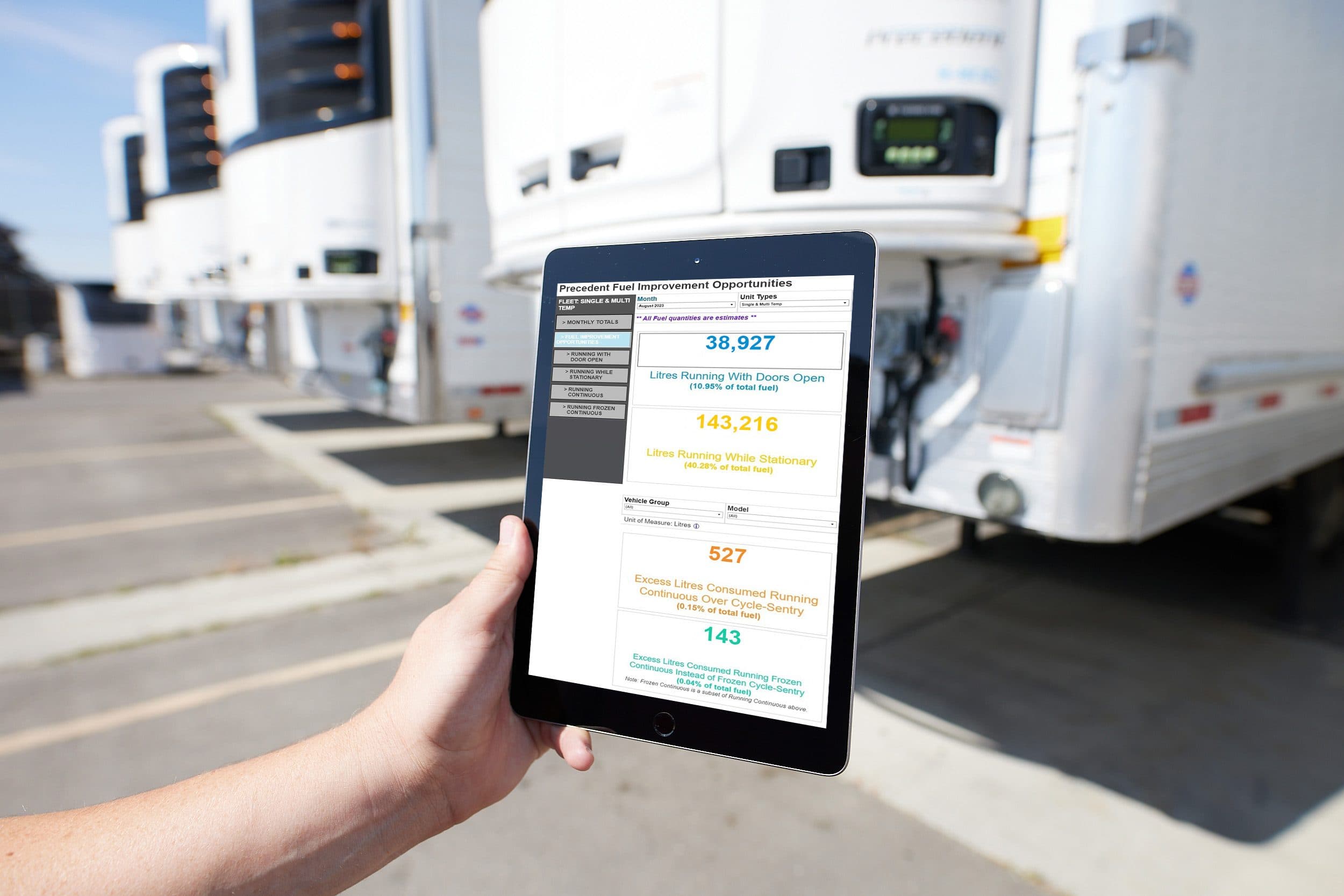 A tablet showing TracKing Pro energy-use figures beside a row of trailers with Thermo King units