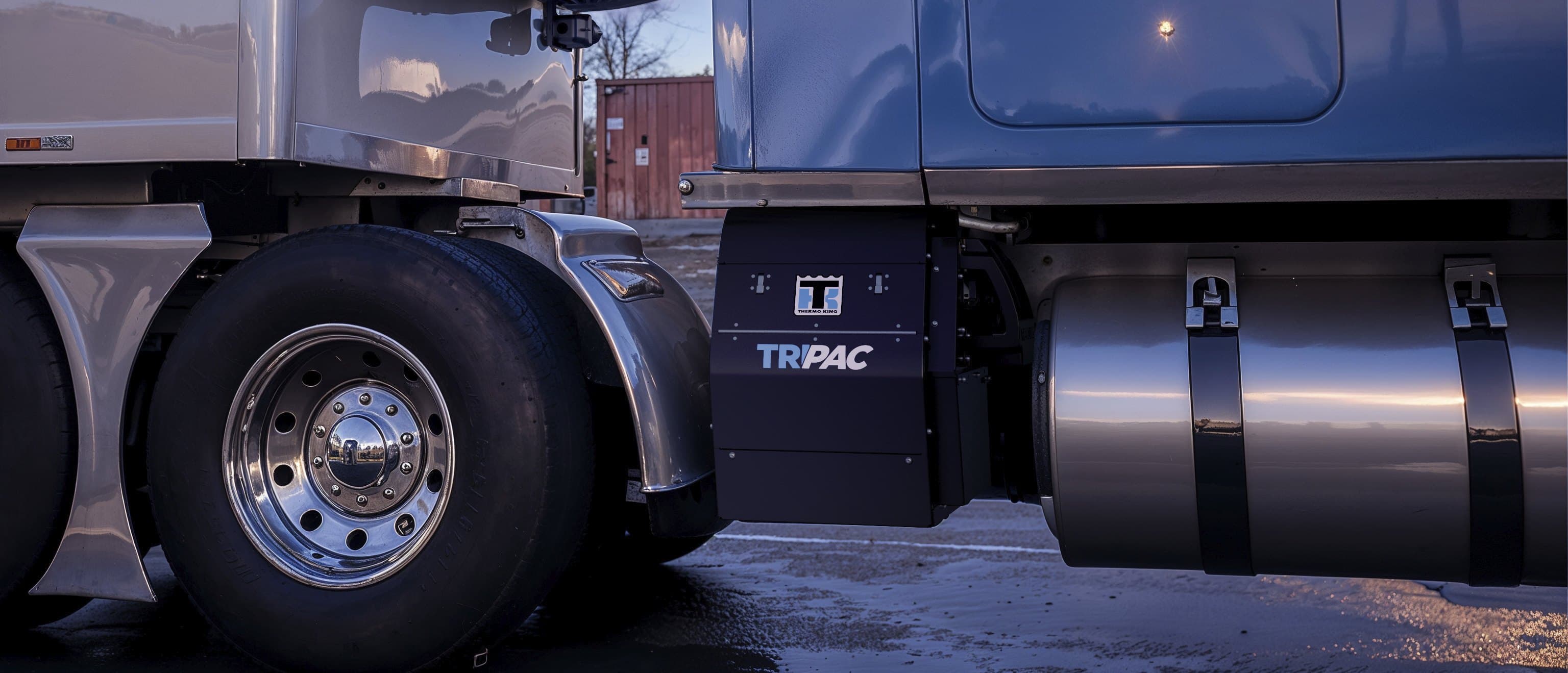 A Thermo King 3rd Generation TriPac APU mounted behind a tractor's fuel tank, beside a reefer trailer
