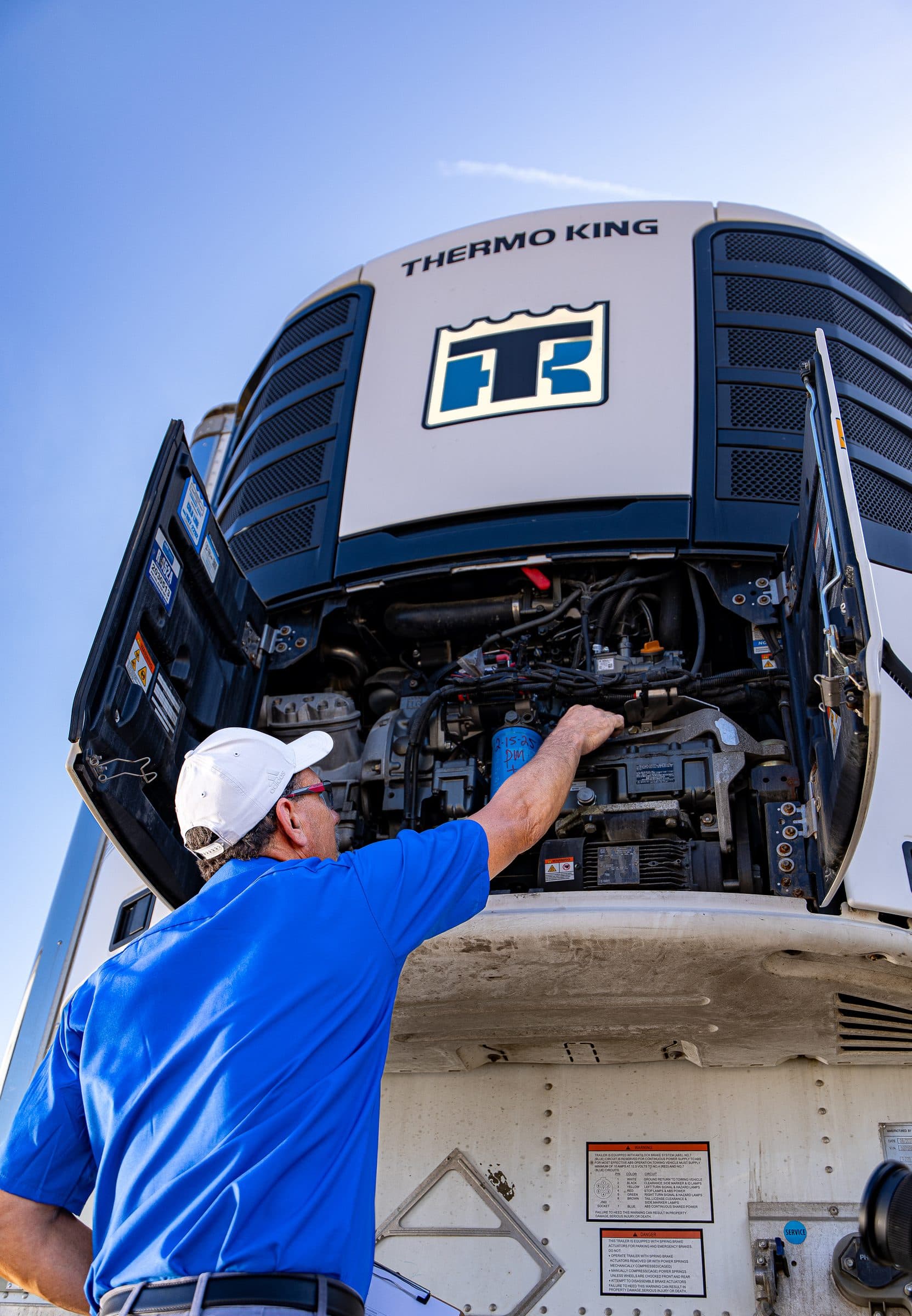 A technician working on an opened-up Thermo King trailer unit, seen from below