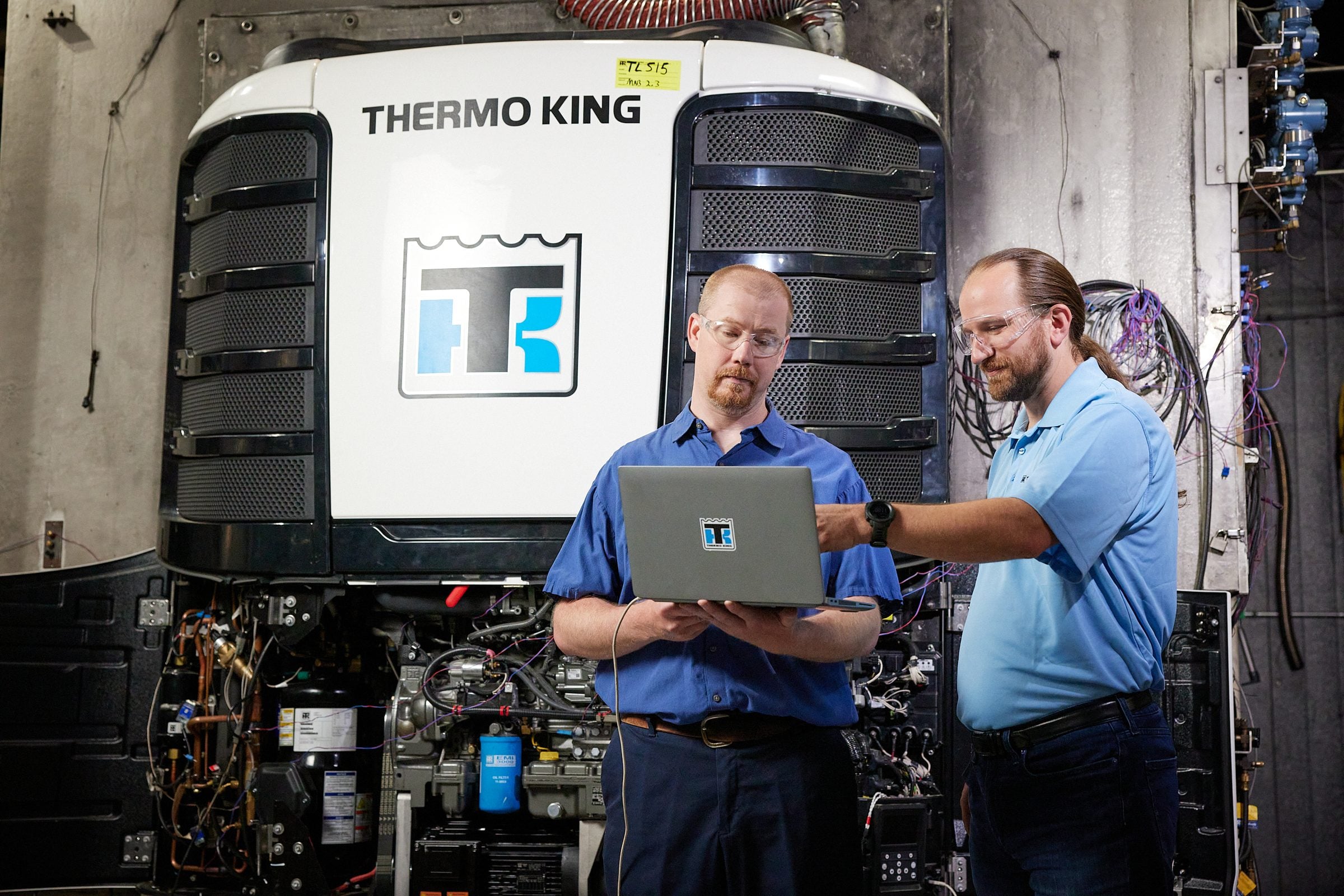 Two technicians reading a laptop in front of an open Thermo King unit